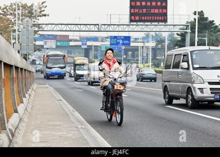 GUANGZHOU-FEB. 21, 2012. Cheerful Chinese girl riding an electric bike on a busy road. Stock Photo