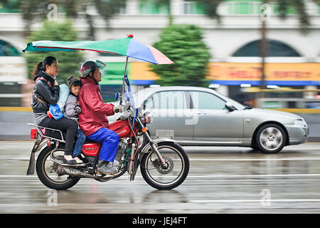 GUANGZHOU-FEB. 25, 2012. Motorcycle taxi in the rain with two passengers with urban scene in motion blur on the background. Stock Photo