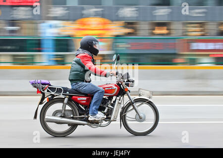 GUANGZHOU-FEB. 25, 2012. Man on a motorcycle on the road with urban scene in motion blur on the background. Stock Photo