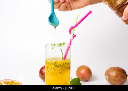 Female hand adding honey in passion fruit juice Stock Photo