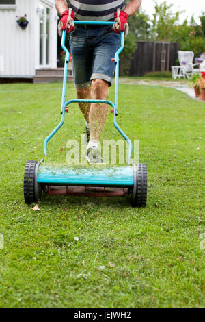 Low front view of man mowing lawn with hands on mower Stock Photo - Alamy