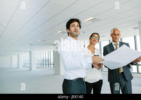 business people and real estate broker discussing over blueprint of empty office space. Real estate agent showing new office space to potential client Stock Photo