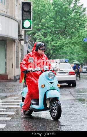 Chinese man in red rainwear on a retro scooter. Shanghai has a humid subtropical climate, its summer is very warm and humid. Stock Photo