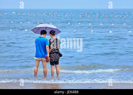 YANTAI-CHINA-JULY 17, 2013. Couple under umbrella enjoys the sea. Because of its weather, coasts and tourist sites it is a popular travel destination. Stock Photo