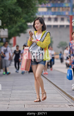 BEIJING-JUNE 9, 2015. Fashionable young Chinese girl busy with her smartphone in the city center of Beijing. Stock Photo