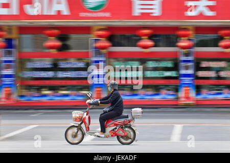 SHANGHAI–MAY 28. Masked woman on an e-bike. At least 120 million e-bikes are already on Chinese roads, and sales are only growing. Stock Photo