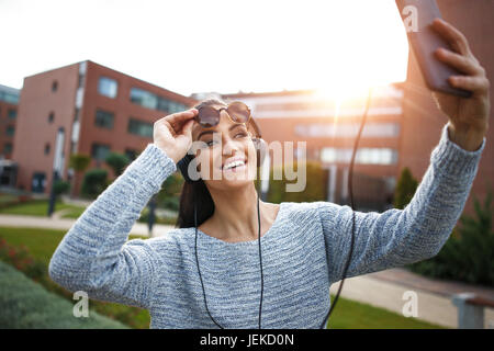 Young woman taking selfie by tablet in city, outdoor in sunset Stock Photo