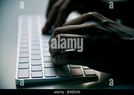 closeup of a young man typing in a computer keyboard in gloom, with a dramatic effect Stock Photo