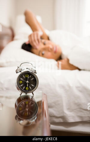 Alarm clock against brunette on bed Stock Photo
