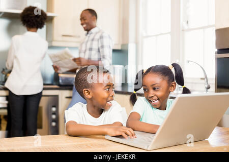 Siblings using laptop in kitchen Stock Photo