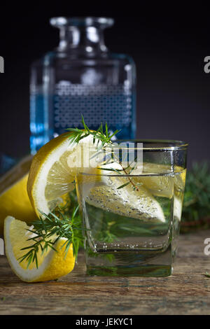 Cocktail with blue gin , tonic and lemon on a old wooden table . Alcoholic drink with lemon slices and juniper branch. Stock Photo
