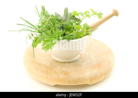 A selection of herbs inside a cream mortar with pestle, standing on light wood chopping board which shows signs of wear.  Isolated against white backg Stock Photo