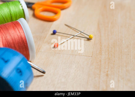Close up of sewing items, cut off at left side of frame with three colourful pins in centre of frame.  These are placed on a birch wood table, which p Stock Photo