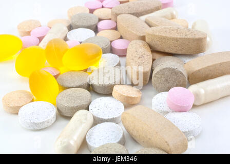 A mixture of different vitamin supplement pills, scattered on a white surface.  Includes hard tablets in various colours, also plastic and gel capsule Stock Photo