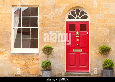 Red wooden doors in an old traditional English stone cottage with two plant pots in front . Stock Photo