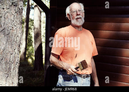 Senior man with paintbrush in front of wooden building Stock Photo