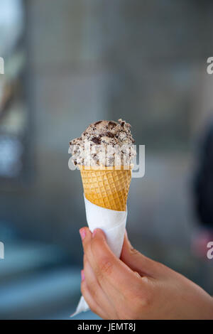 Female hand holding out cone with chocolate ice cream with cookies Stock Photo