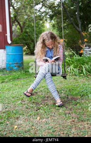 Girl on swing reading book Stock Photo