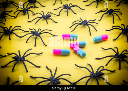 Spiders around capsules on yellow background, concept phobia to medicines Stock Photo