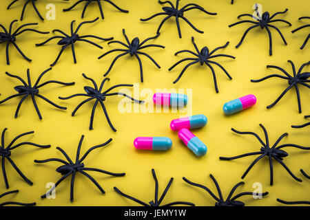 Spiders around capsules on yellow background, concept phobia to medicines Stock Photo