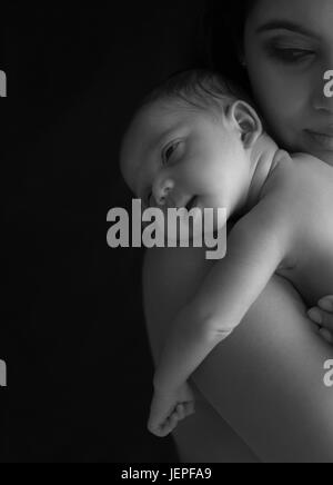 Model released photograph of a newborn baby boy smiling while resting his head on his mothers shoulders Stock Photo