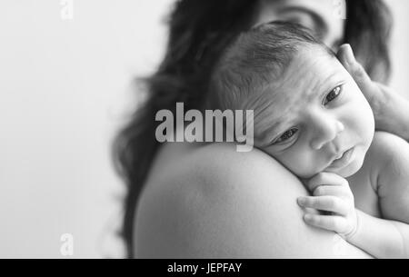 Model released photograph of a newborn baby boy with expressive eyes is resting on his mothers shoulders Stock Photo