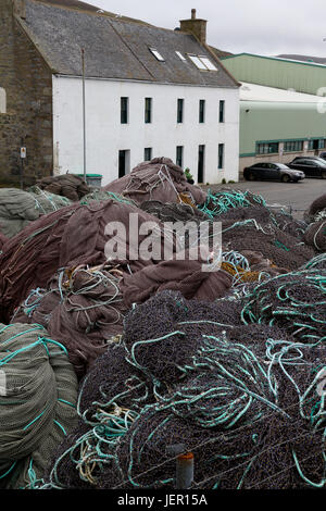 Mounds of purple fishing nets with turquoise ropes piled up in front of a white house by Scalloway harbor, Shetland, Scotland on overcast day. Stock Photo
