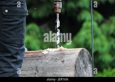 The worker collects the frame and drills a hole in a log for dowel using a drill when building a wooden house Stock Photo