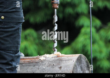 The worker collects the frame and drills a hole in a log for dowel using a drill when building a wooden house Stock Photo
