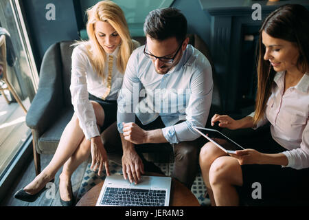 Three young smiling cheerful colleagues working together on laptop Stock Photo