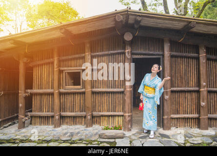 Beauty girl wearing traditional kimono in front of old wooden house. Japaneses enjoying sunshine after rain, asian woman looking up at clearing sky ch Stock Photo