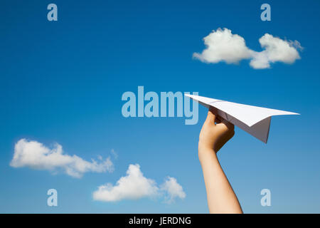 Paper plane in child hand on blue sky and clouds background. (With space for text.) Stock Photo