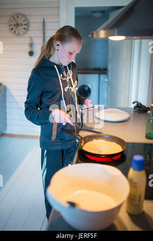 Teenage girl making pancakes while listening music Stock Photo