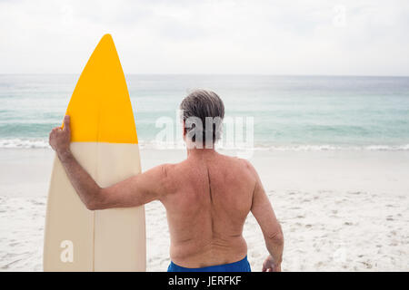 Senior man standing on beach with surfboard Stock Photo