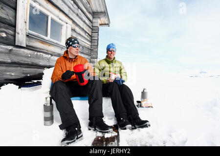 Couple resting in front of mountain cabin Stock Photo