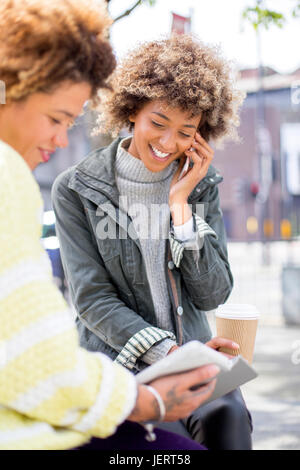 Two women in the city. One is using a digital tablet and the other is talking on the phone. Stock Photo