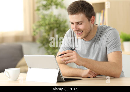 Casual man searching on line using a tablet with a pen sitting in a desk at home with a window in the background Stock Photo