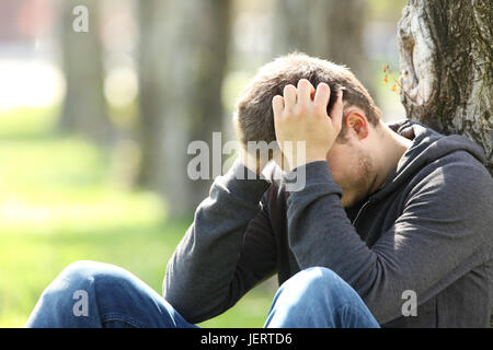 Portrait of a single sad teen lamenting sitting on the grass in a park Stock Photo