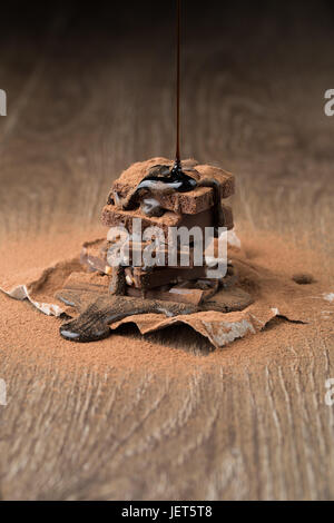 Pyramid of chocolate with syrup on wooden table with cocoa powder on black background Stock Photo