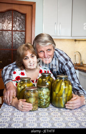 Smiling Caucasian aged couple sitting in domestic kitchen with glass cans with picklers Stock Photo