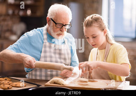 grandchild and grandfather cooking and making dough for cookies with kitchen utensils at kitchen table, cooking in kitchen concept Stock Photo