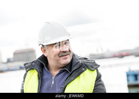 Senior engineer builder at the construction site in a port. Wearing safety helmet and yellow vest. Stock Photo