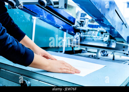 Worker preparing print screening metal machine. Industrial printer. Manufacture work. Side view. Stock Photo