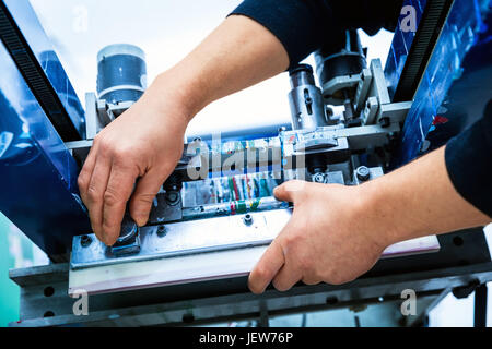 Worker preparing print screening metal machine. Industrial printer. Manufacture work. Stock Photo