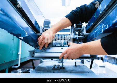 Worker preparing print screening metal machine. Industrial printer. Manufacture work. Stock Photo