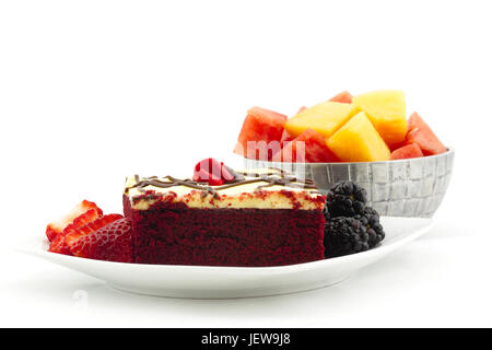Square cut of iced red velvet cake with berries and metal bowl filled with cubes of watermelon and cantaloupe.  Summer dessert in horizontal image wit Stock Photo