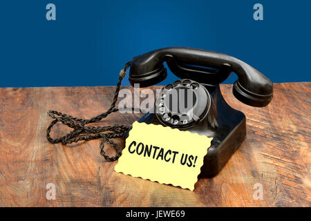 Vintage Phone on Wooden Table with Contact Us Card. Stock Photo