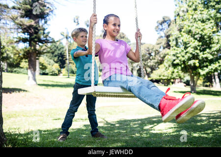 Boy pushing his sister on swing Stock Photo
