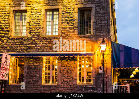 Montreal, Canada - May 27, 2017: Old town area brick building illuminated by yellow lights and lanterns by street in evening outside in Quebec region  Stock Photo