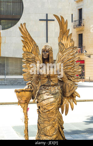 Barcelona, Spain - May 25, 2017: Street actress dressed as a golden angel on Ramblas with a church at the background in Barcelona, Spain. Stock Photo